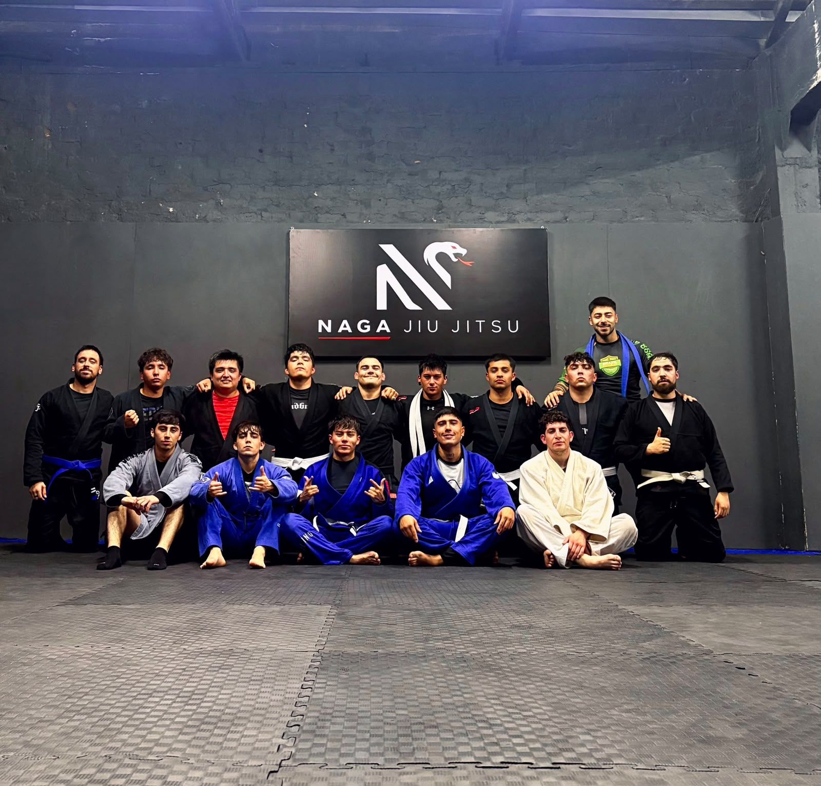 Grupo de alumnos y profesores con kimono bajo el letrero de Naga Jiu Jitsu